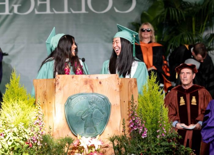Two students at Commencement podium facing each other and smiling