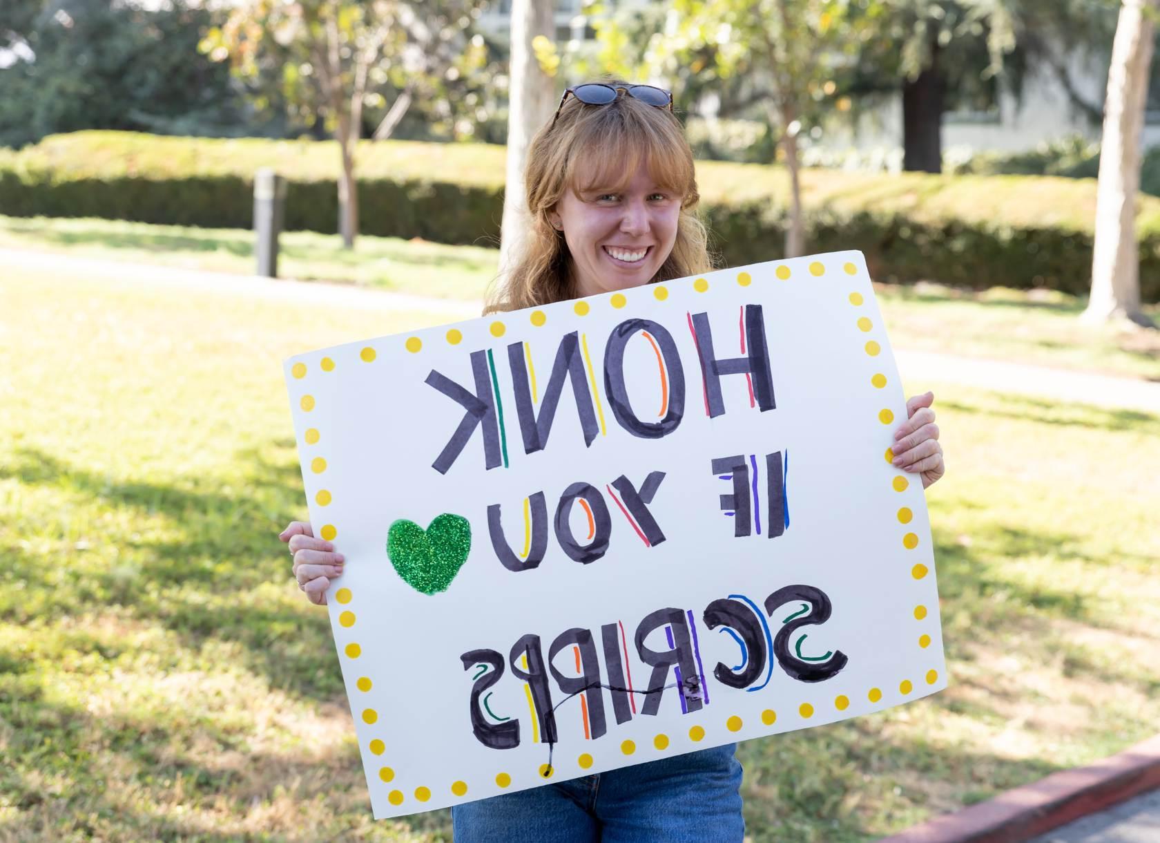 Student smiling carrying sign that reads honk if you love Scripps